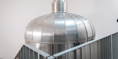 Eine glänzende, silberne Kuppel aus Metall steht in einem modernen Raum, umgeben von einem minimalistischen Geländer.