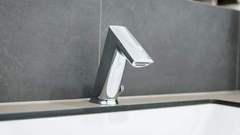 Ein moderner Wasserhahn aus glänzendem Metall, der elegant über einer weißen Badewanne positioniert ist.