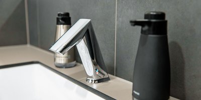 Ein moderner Wasserhahn aus glänzendem Metall steht neben einem schwarzen Seifenspender auf einer hellen Arbeitsplatte.