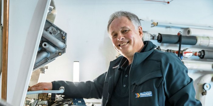 Ein lächelnder Techniker steht neben einer Maschine und arbeitet an einem Rohrsystem in einem hellen, modernen Raum.