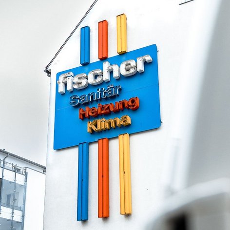 Das auffällige Schild von Fischer zeigt Dienstleistungen in Sanitär, Heizung und Klima in leuchtenden Farben.
