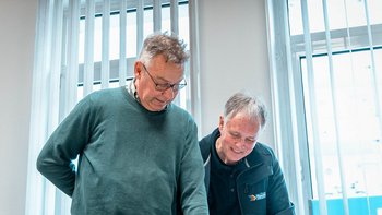 Zwei Männer stehen an einem Tisch und betrachten aufmerksam Dokumente, während sie in einem hellen Raum arbeiten.