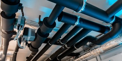 Dunkle Rohre verlaufen über eine Decke, während elektrische Komponenten und Kabel sichtbar sind, die eine technische Umgebung schaffen.
