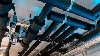 Dunkle Rohre verlaufen über eine Decke, während elektrische Komponenten und Kabel sichtbar sind, die eine technische Umgebung schaffen.