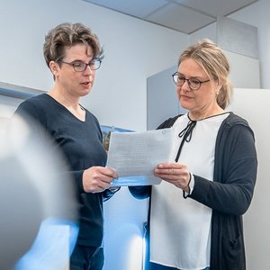 Zwei Frauen stehen in einem modernen Büro und besprechen ein Dokument, während sie sich aufmerksam ansehen.