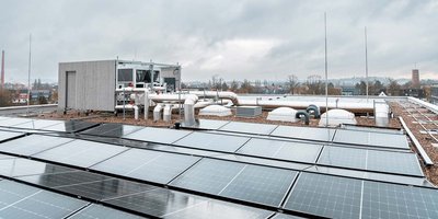 Auf dem Dach sind zahlreiche Solarpanels zu sehen, die in der grauen Umgebung glänzen, während Wolken den Himmel bedecken.