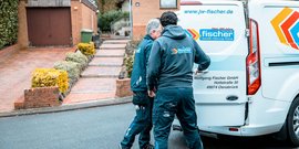 Zwei Handwerker in Arbeitskleidung laden Ausrüstung aus einem weißen Firmenfahrzeug in einer Wohngegend aus.
