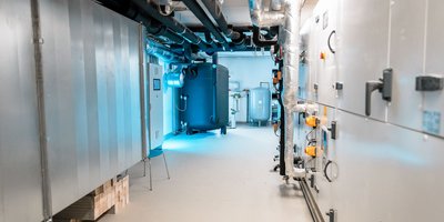 Ein langer, heller Gang mit großen Maschinen und Rohren, die an den Wänden entlang verlaufen, schafft eine technische Atmosphäre.