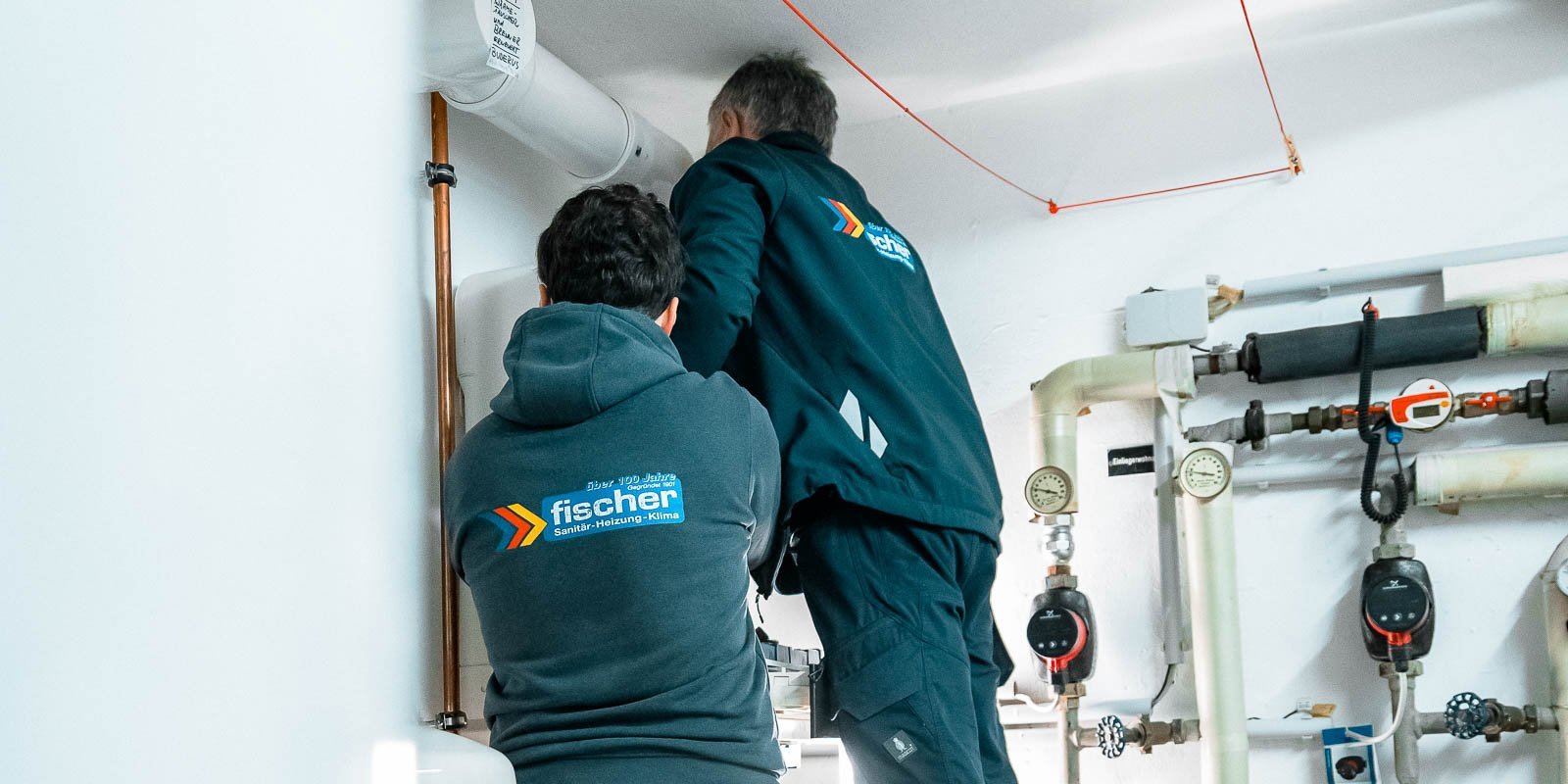 Zwei Techniker arbeiten an einer Rohrinstallation, einer steht auf einer Leiter und der andere beobachtet aufmerksam.