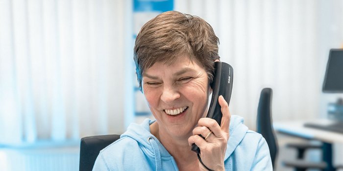 Eine Frau mit kurzem Haar lächelt, während sie ein Telefon in der Hand hält und ein Gespräch führt.