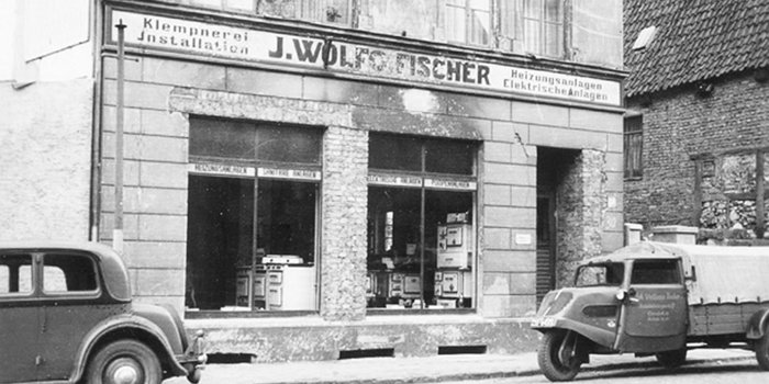 Das historische Geschäft von J. Wolf Fischer zeigt eine Fassade mit Schaufenstern, die Heizungsanlagen und Elektrogeräte präsentieren.