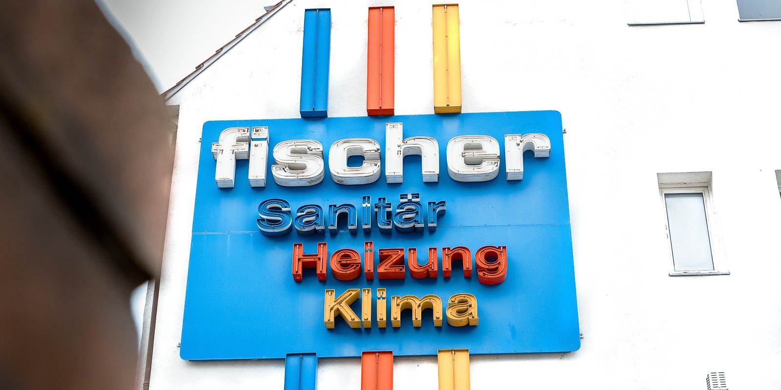 Ein leuchtendes Schild mit dem Namen 'fischer', das Dienstleistungen in Sanitär, Heizung und Klima bewirbt.
