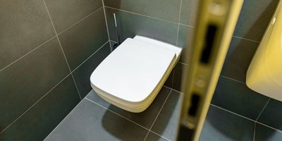 Ein modernes, weißes WC steht in einem stilvollen, gefliesten Badezimmer mit grauen Fliesen und minimalistischer Ausstattung.