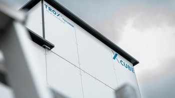 Ein modernes Gebäude mit einer weißen Fassade und dem Schriftzug 'TROX' in blauer Schrift, unter einem bewölkten Himmel.